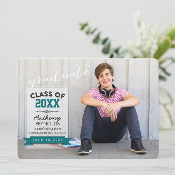 Smiling graduate sitting against a wall.